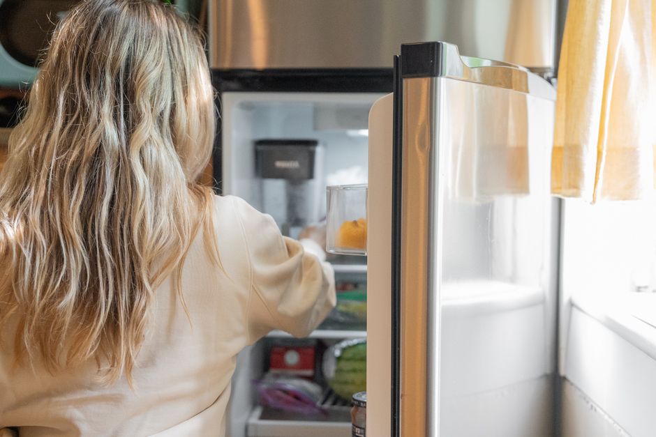 Persona abriendo la puerta de un frigorífico lleno de comida en la cocina