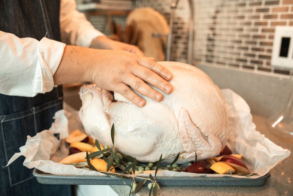 Persona colocando un pavo crudo sobre una bandeja de horno con frutas y hierbas