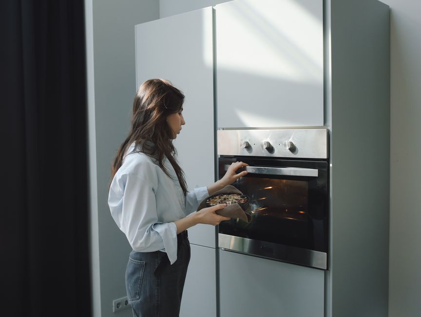 Persona metiendo una bandeja con comida en un horno eléctrico empotrado de una cocina moderna
