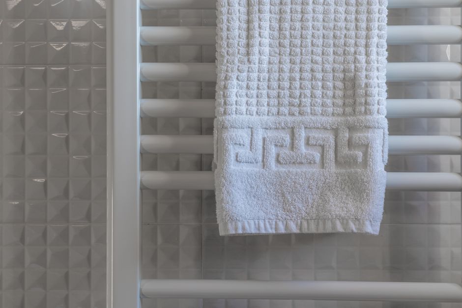 Toalla blanca colgada de un toallero blanco de barras en un baño de azulejos claros