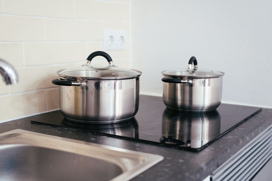 Dos ollas de acero inoxidable con tapa sobre una placa de cocina eléctrica negra