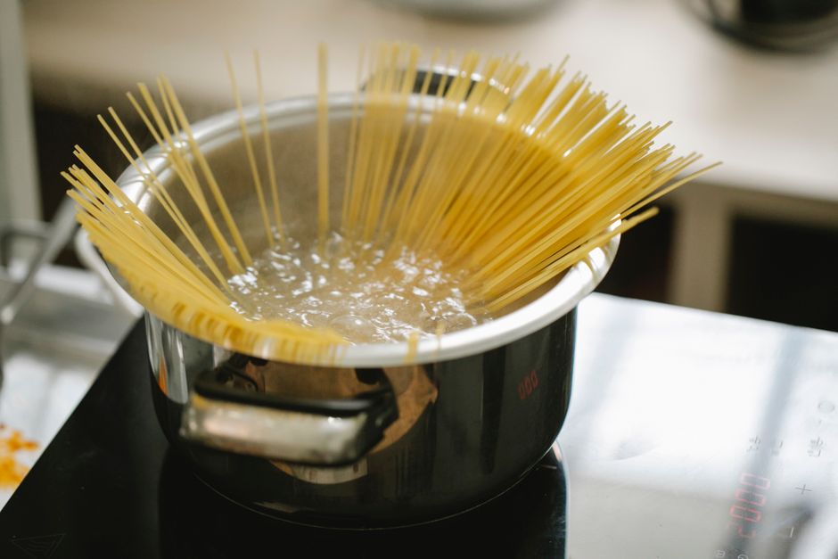 Espaguetis cociéndose en una olla de agua hirviendo sobre una placa eléctrica negra