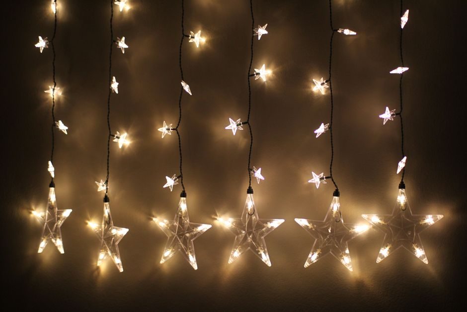Cortina de luces cálidas con estrellas colgando de una pared oscura